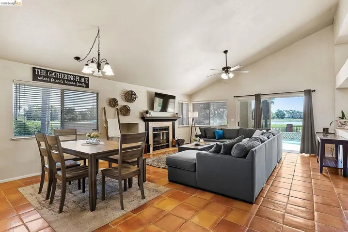 Dining space featuring light tile patterned flooring, a ceiling fan, a chandelier, a tiled fireplace, and high vaulted ceiling