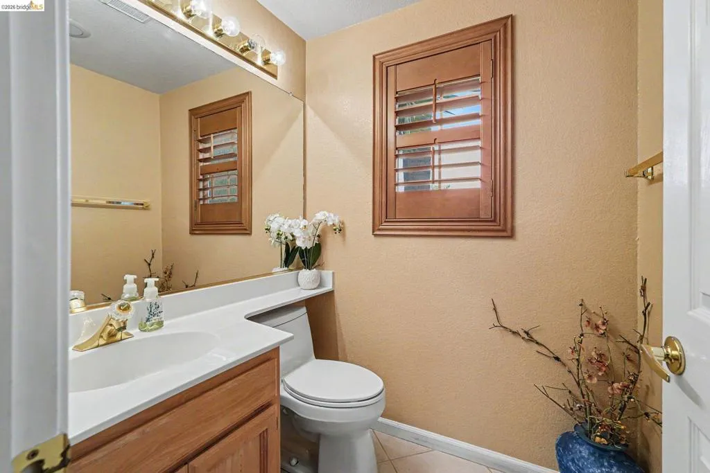 Full-length vanity mirror with a three-bulb light fixture, wood-finish vanity with an integrated sink, white countertop, and a wood-framed window with plantation shutters