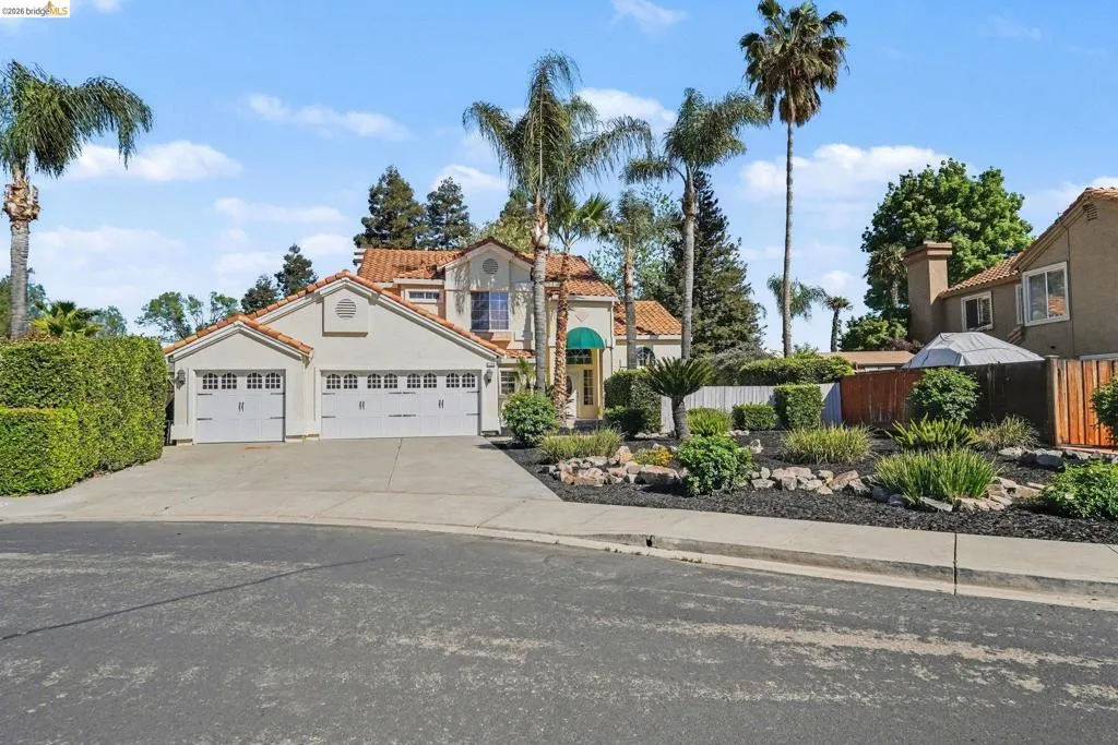 Stucco exterior residence featuring a tile roof, a three-car garage with individual doors, a concrete driveway, and mature palm trees