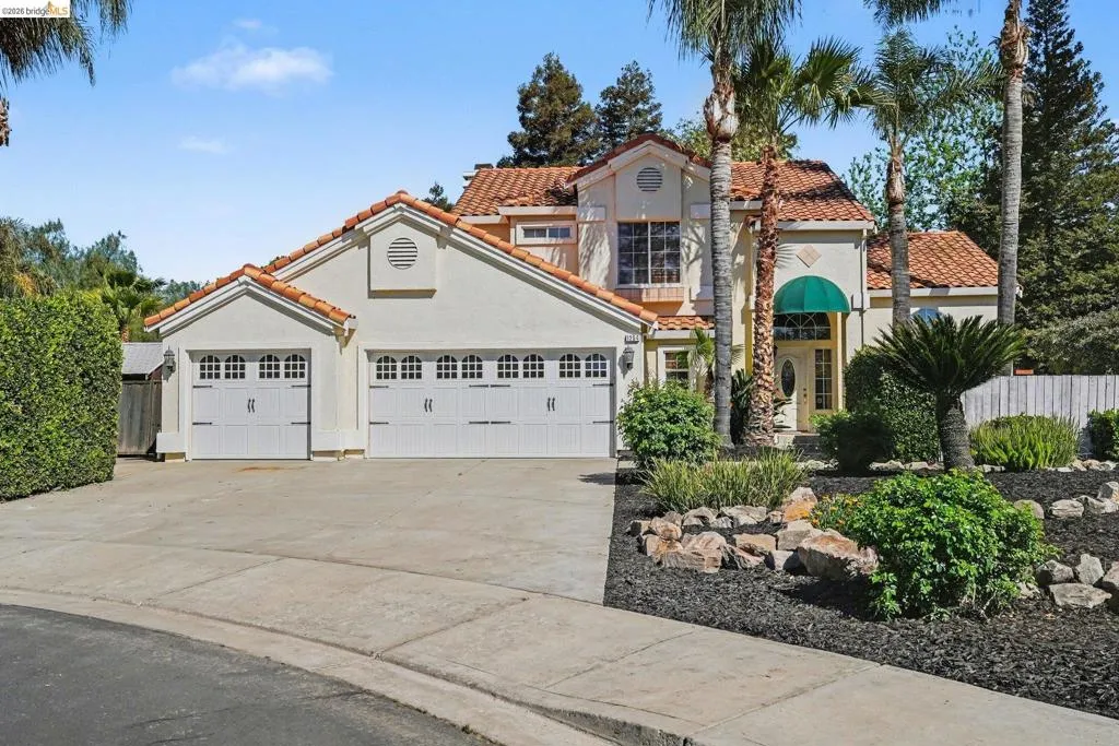 Stucco exterior featuring a red tile roof, two-car garage, and a lush, landscaped front yard with palm trees