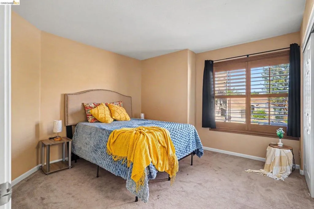 Bedroom featuring wall-to-wall carpeting, a large window with wood-finish blinds, and a built-in closet with bifold doors