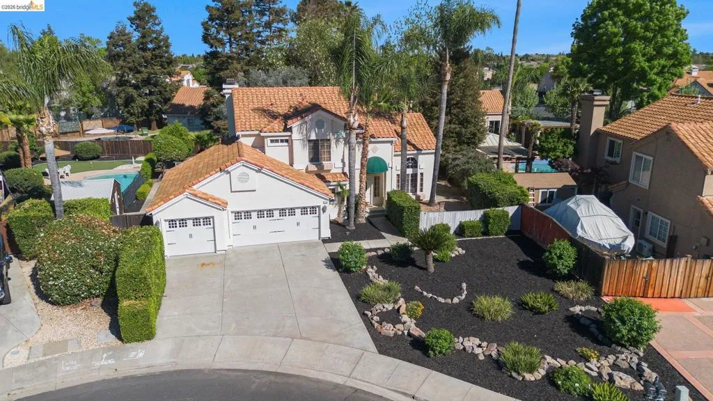 Mediterranean-style residence featuring a tile roof, stucco exterior, three-car garage, mature landscaping, and an inground swimming pool