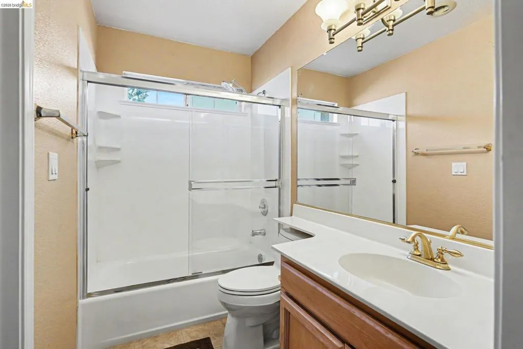Bathroom featuring a full-size bathtub with sliding glass doors, a vanity with an integrated sink and countertop, and a wall-mounted mirror