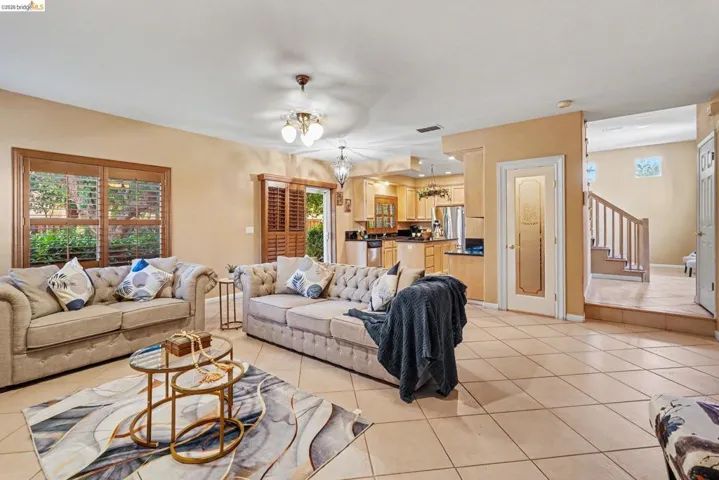 Spacious open-concept living area featuring large windows with wood plantation shutters, neutral-toned tile flooring, and integrated ceiling lighting