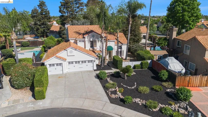 Mediterranean-style residence featuring a tile roof, stucco exterior, three-car garage, mature landscaping, and an inground swimming pool