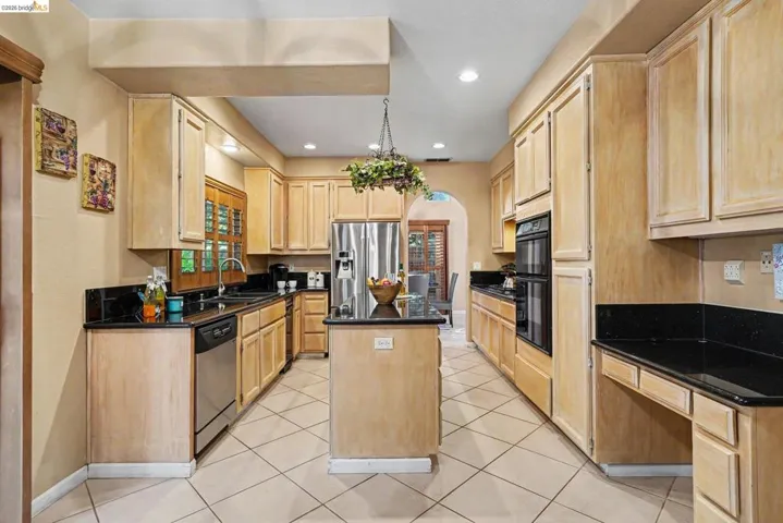 Spacious kitchen featuring extensive light wood cabinetry, black countertops, a central island, recessed lighting, and tile flooring