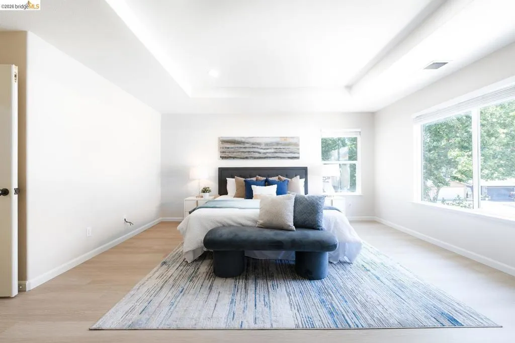 Bedroom featuring a tray ceiling with recessed lighting, light wood-finish flooring, and large windows