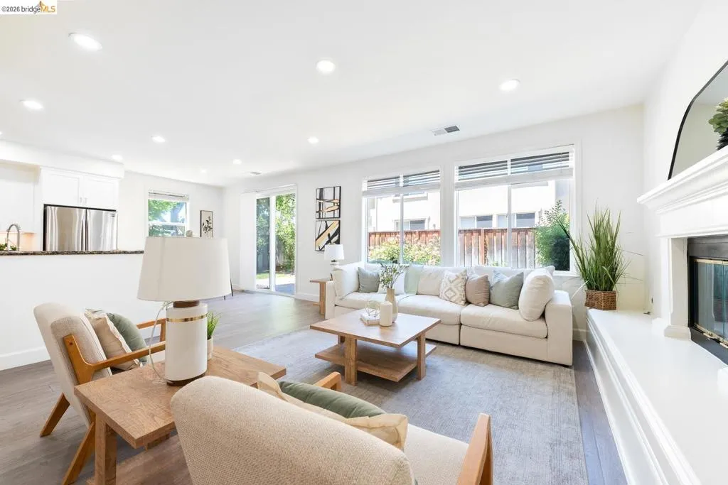 Spacious living area featuring large windows, wood-finish flooring, recessed lighting, and a white mantel