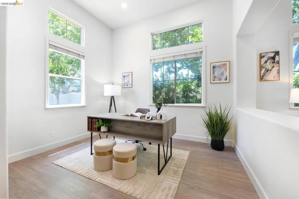 Room featuring high ceilings, multiple windows, recessed lighting, wood-finish flooring, and white baseboards
