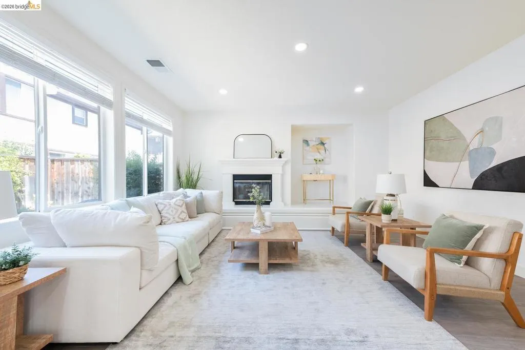 Bright living space featuring a fireplace with a white mantel, large windows with blinds, wood-finish flooring, recessed lighting, and a neutral color palette