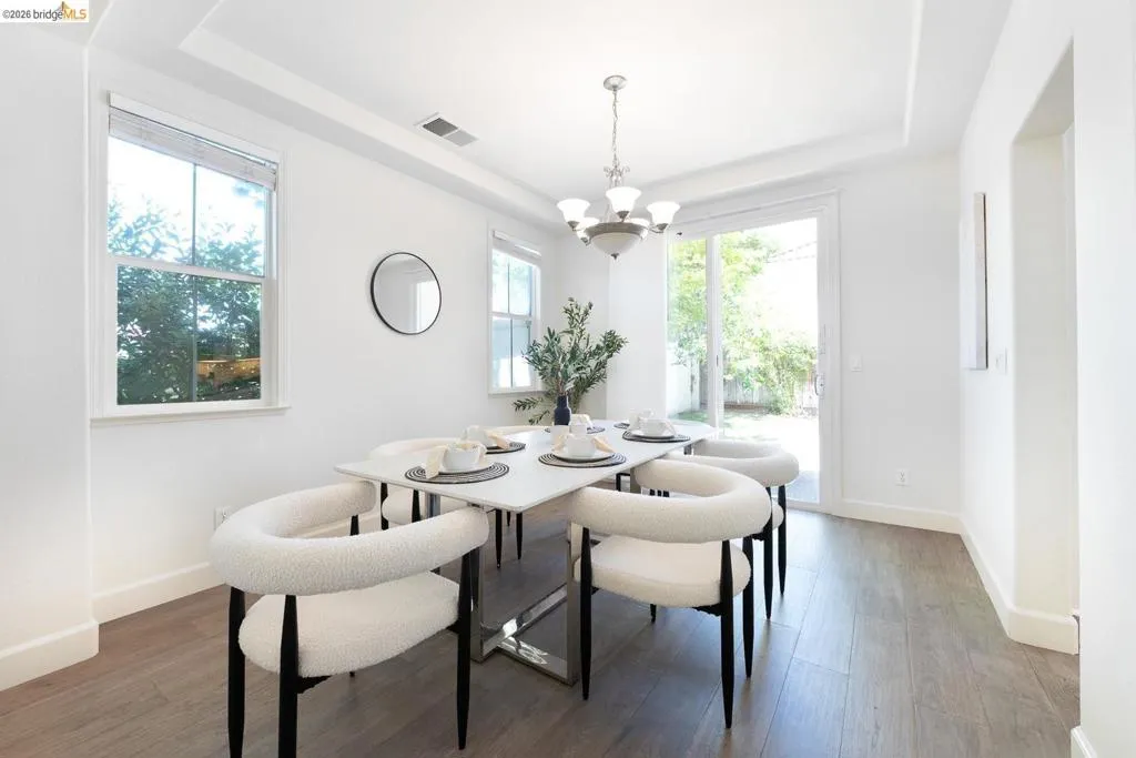 Dining area featuring wood-finish flooring, two large windows, a sliding glass door, a tray ceiling, and a five-light chandelier