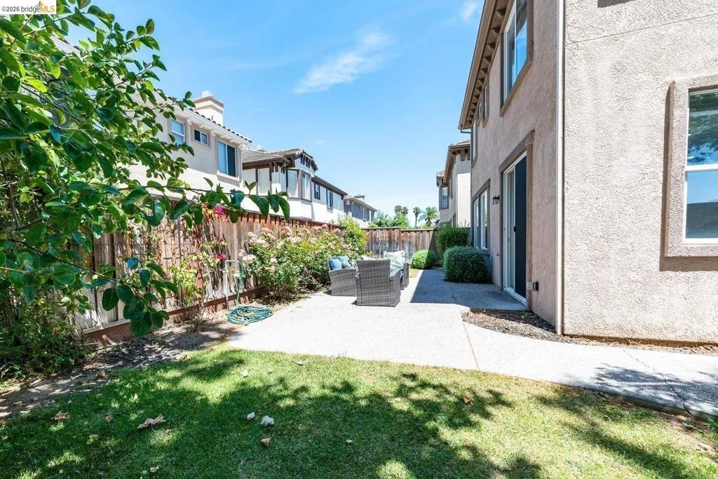 Expansive backyard featuring a concrete patio, a section of lawn, and a wood fence with established flowering shrubs