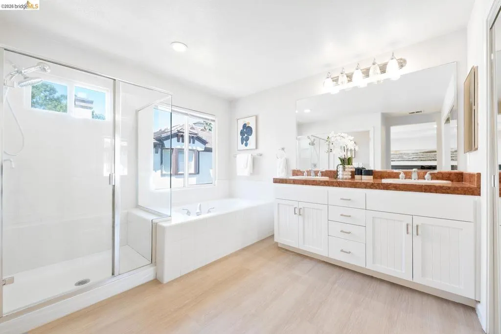 Spacious bathroom featuring a dual vanity with a brown stone countertop, white cabinetry, and undermount sinks