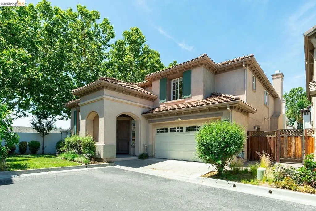 Stucco exterior featuring a red tile roof, arched entryway, attached garage, and decorative window shutters