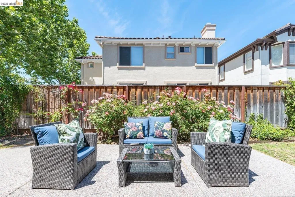 Expansive backyard patio featuring a concrete surface, a wood fence, and mature flowering shrubs