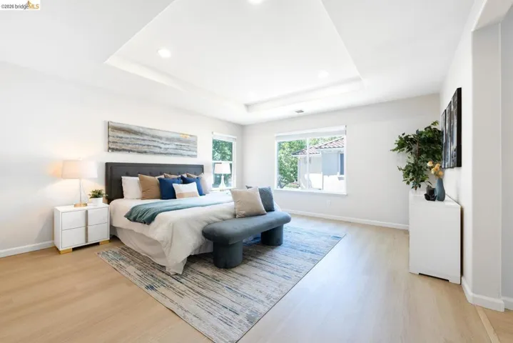 Spacious room featuring a tray ceiling with recessed lighting, light wood-finish flooring, and a large window