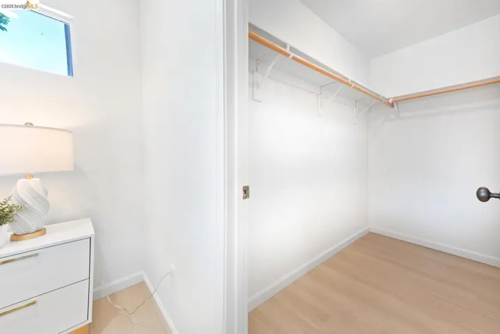 Walk-in closet with light wood-finish flooring, white walls, and dual wood hanging rods