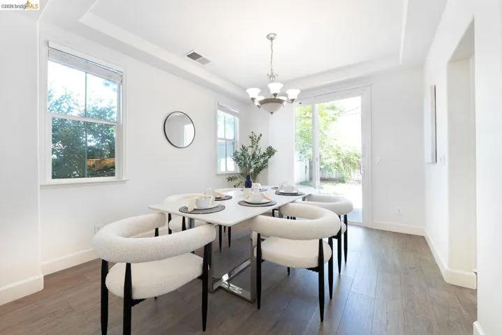 Dining area featuring wood-finish flooring, two large windows, a sliding glass door, a tray ceiling, and a five-light chandelier