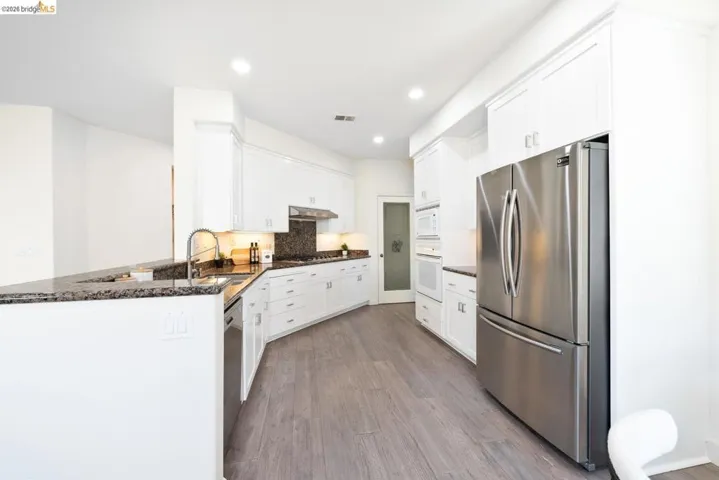 Spacious kitchen featuring white cabinetry, granite countertops, wood-finish flooring, stainless steel appliances, and recessed lighting