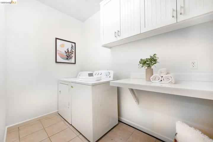 Laundry area featuring tiled flooring, white walls, built-in shelving, white upper cabinetry, and a white countertop