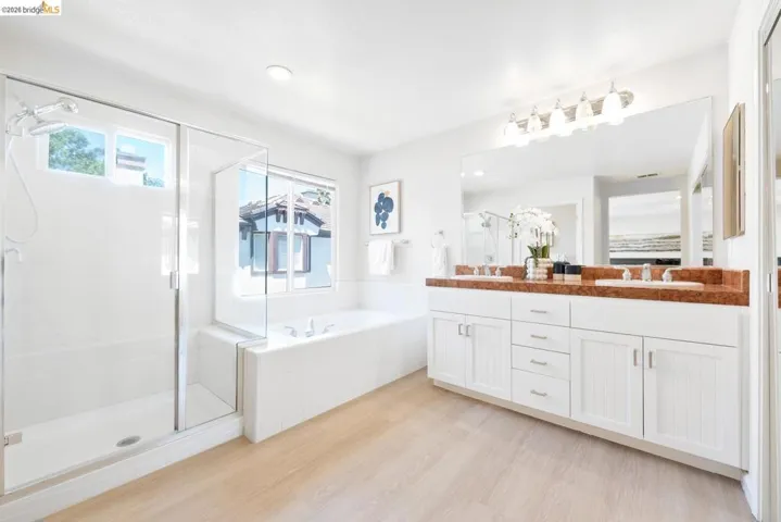 Spacious bathroom featuring a dual vanity with a brown stone countertop, white cabinetry, and undermount sinks