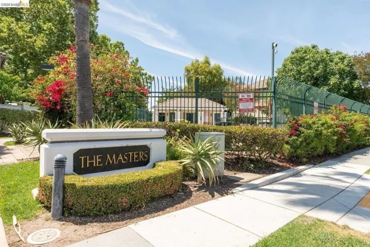 Community signage featuring "THE MASTERS" with manicured shrubbery, a perimeter fence, and mature trees