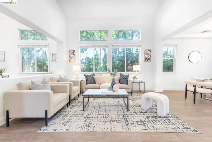Light-filled living area featuring vaulted ceilings, abundant windows, wood-finish flooring, and crisp white walls