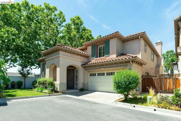 Stucco exterior featuring a red tile roof, arched entryway, attached garage, and decorative window shutters