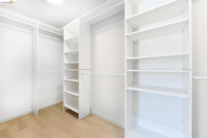 Expansive walk-in closet featuring light wood-finish flooring, white walls, and a ceiling-mounted light fixture
