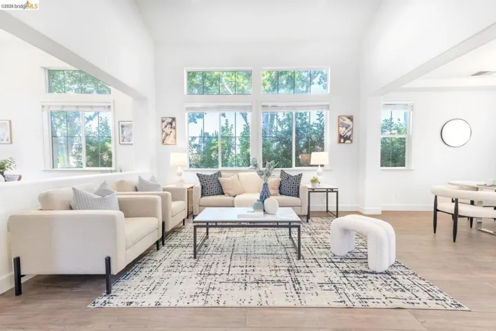 Light-filled living area featuring vaulted ceilings, abundant windows, wood-finish flooring, and crisp white walls