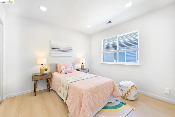 Bright room featuring a large window with horizontal blinds, light wood-finish flooring, recessed lighting, white baseboards, and a white interior door