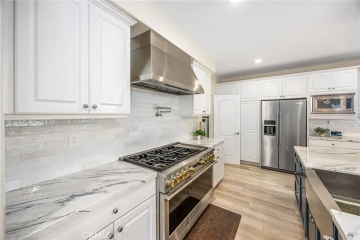 Premium stainless steel appliance suite highlighted by a professional-grade gas range, oversized vent hood, and built-in refrigeration