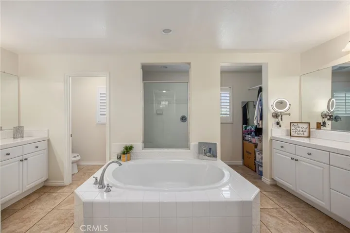 Primary bathroom with dual vanities, soaking tub, separate shower, and walk-in closet access