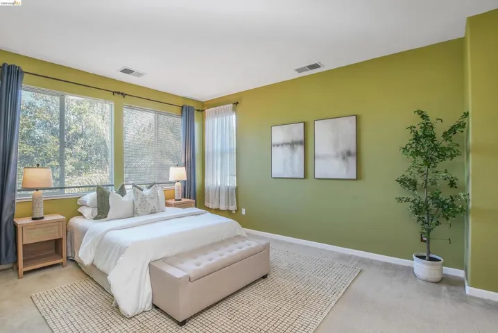 Bedroom featuring a broad window wall with roller shades and full-length drapes, soft carpet flooring, and an accent wall