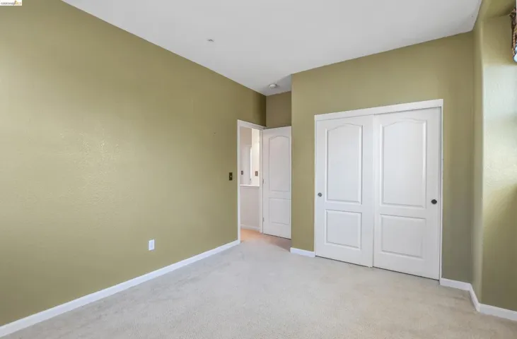 Carpeted room featuring light green walls, white baseboards, and a white bi-fold closet door with black circular hardware