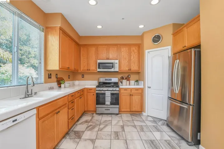 Kitchen featuring light wood cabinetry, stainless steel appliances, and white tile countertops