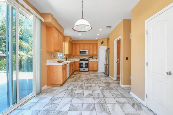 Spacious kitchen featuring light wood cabinetry, white countertops, stainless steel appliances, and large format tile flooring