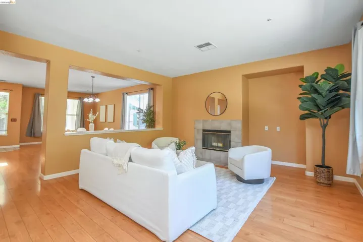 Living area featuring wood-finish flooring, a tiled fireplace, and a large pass-through opening to an adjacent room
