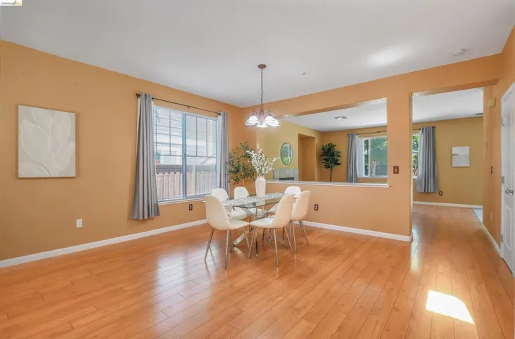 Dining area featuring wood-finish flooring, a contemporary chandelier, and a large window with vertical blinds