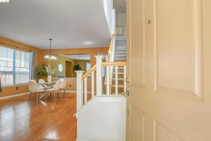 Entryway featuring a paneled door with polished hardware, a carpeted staircase with white balusters and a wood handrail, and wood-finish flooring