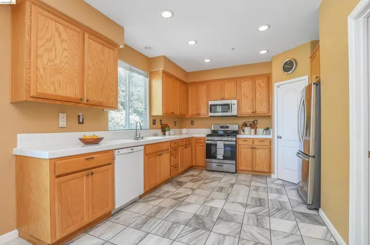 Kitchen featuring wood cabinetry, stainless steel appliances, a window above the sink, recessed lighting, and patterned tile flooring
