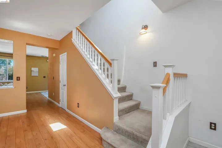 Two-story entryway featuring wood-finish flooring, a carpeted staircase with white balusters and wood handrails, and a transom window