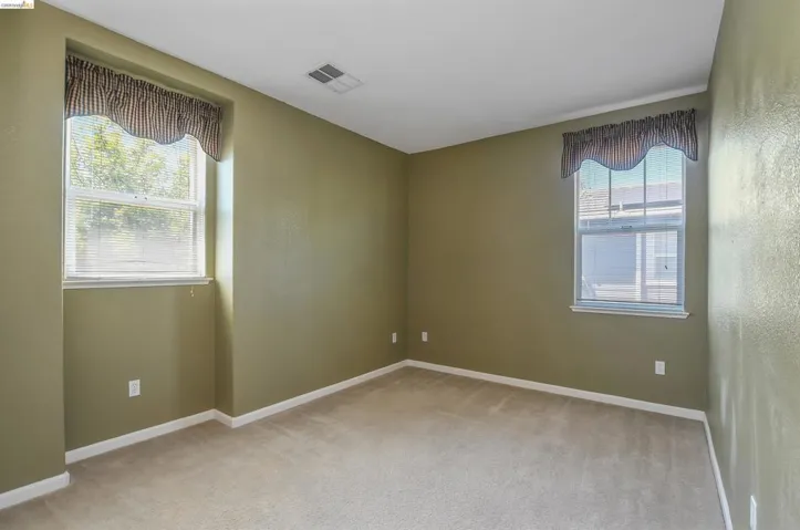 Carpeted interior room featuring two windows with valances and blinds, neutral wall paint, and white trim