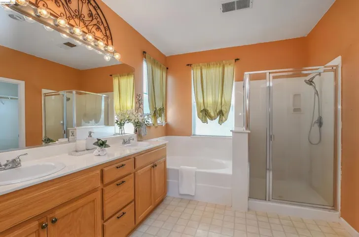 Bathroom featuring a dual vanity with wood cabinetry and undermount sinks, a built-in soaking tub, a separate glass-enclosed shower, and tile flooring