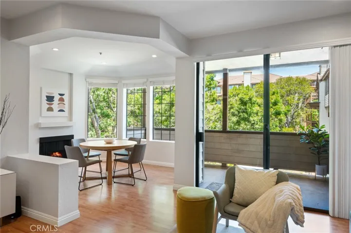 Living area with a cozy fireplace, abundant natural light, and private balcony overlooking mature trees.