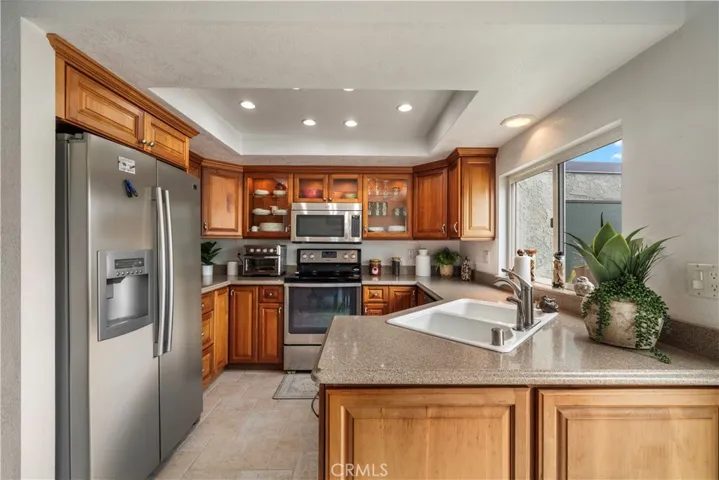 Upgraded kitchen features Silestone countertops, custom solid-wood cabinetry with glass display panels, stanless appliances, and coved ceiling with recessed lighting