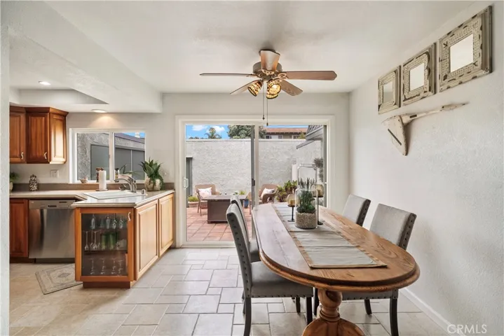Dining room and kitchen with travertine-style title flooring and ceiling fan and sliders that open to private courtyard-style patio