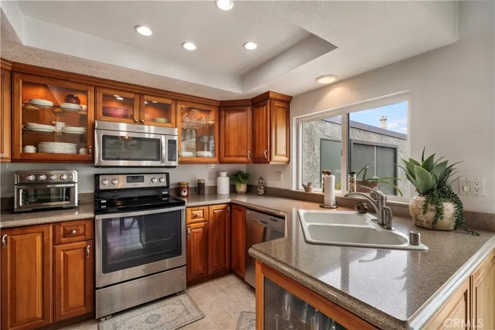 Upgraded kitchen features Silestone countertops, custom solid-wood cabinetry with glass display panels, stanless appliances, and coved ceiling with recessed lighting