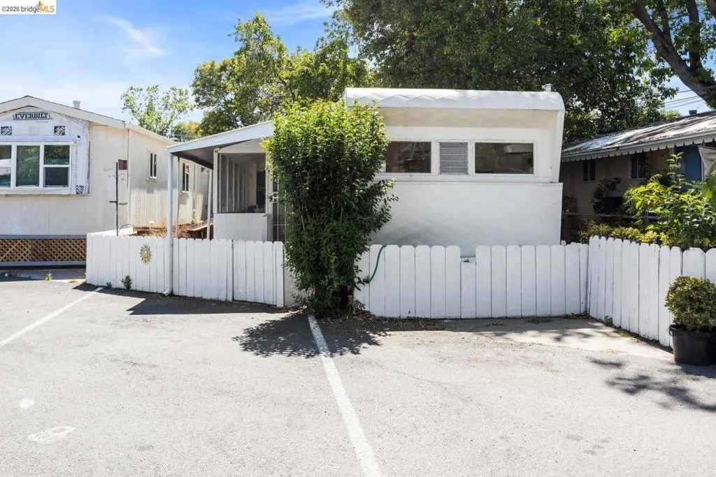 Paved parking area leading to a white picket fence enclosing a compact property