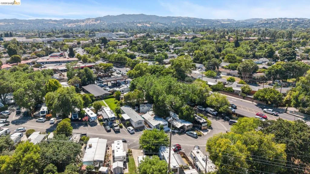 Aerial perspective showcasing a residential and commercial area with abundant mature trees and mountainous terrain in the distance